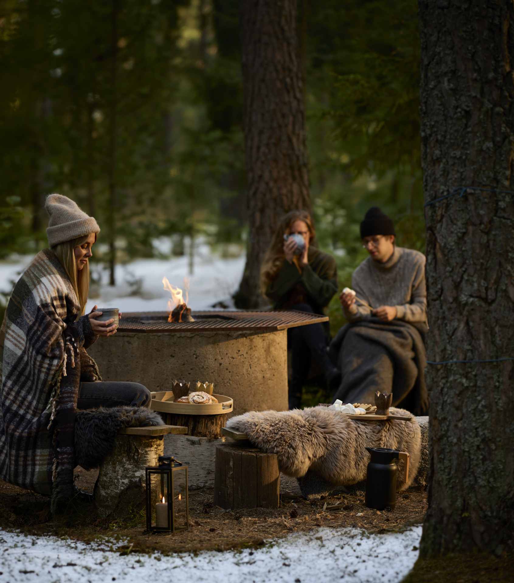 tre personer sittandes runt en eld med fårskinn i fokus
