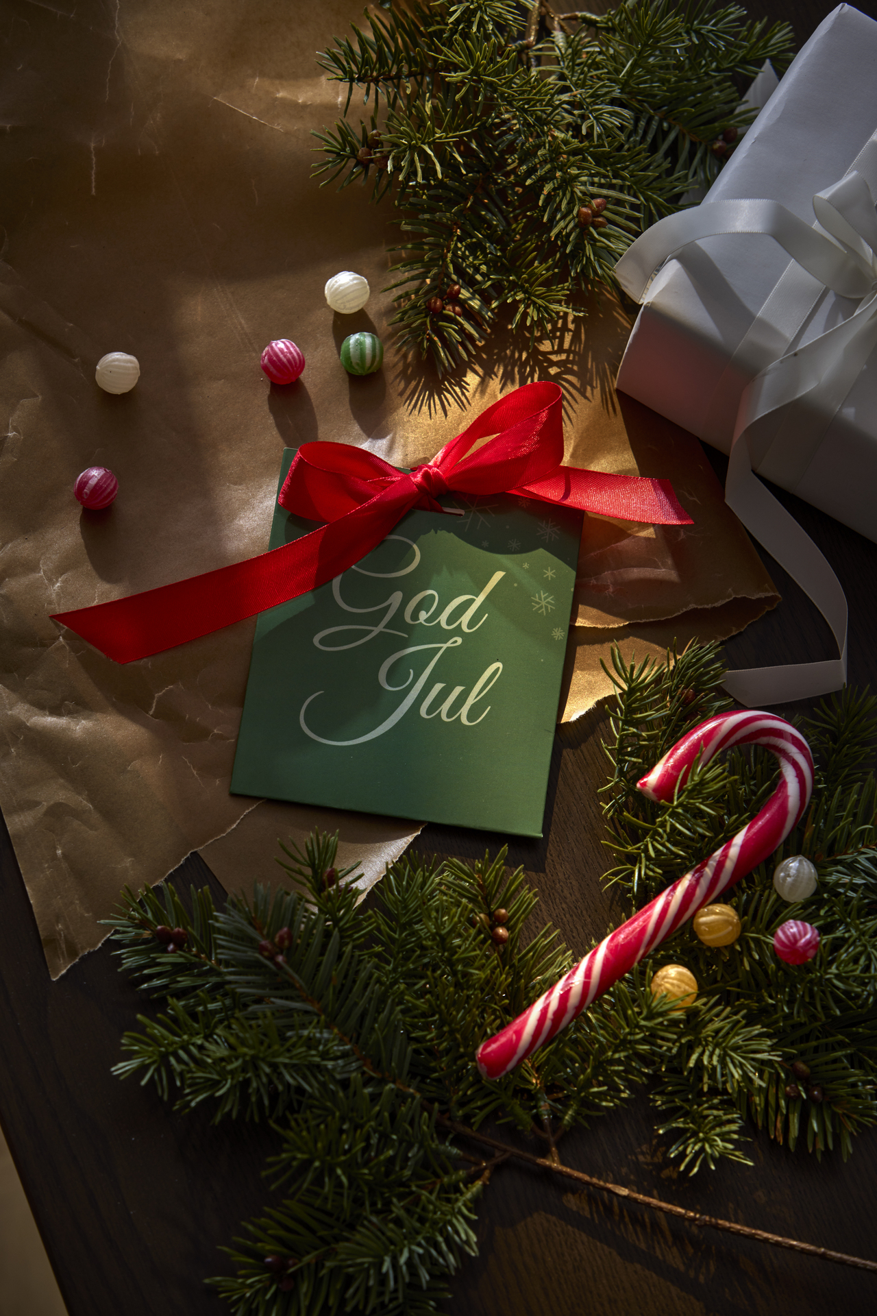 ett presentkort i ett grönt kuvert liggandes på ett bord med granris och julgodis runt om. 