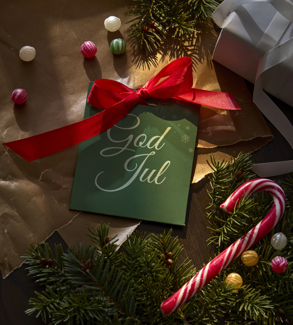 ett presentkort i ett grönt kuvert liggandes på ett bord med granris och julgodis runt om.