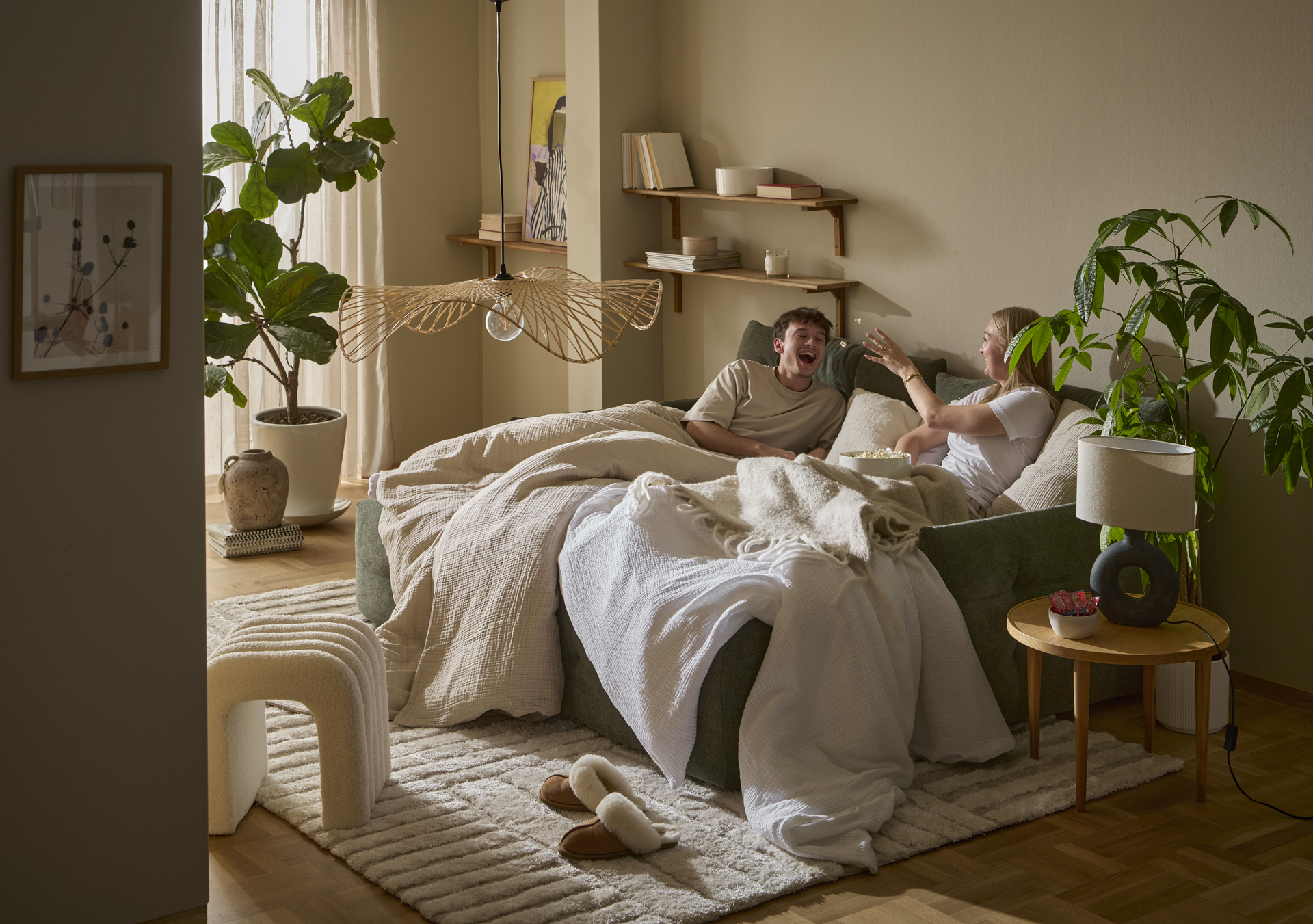 I en grön bäddsoffa sitter en tjej och en kille nedbäddade under ett täcke och kastar popcorn till varandra