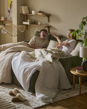 I en grön bäddsoffa sitter en tjej och en kille nedbäddade under ett täcke och kastar popcorn till varandra