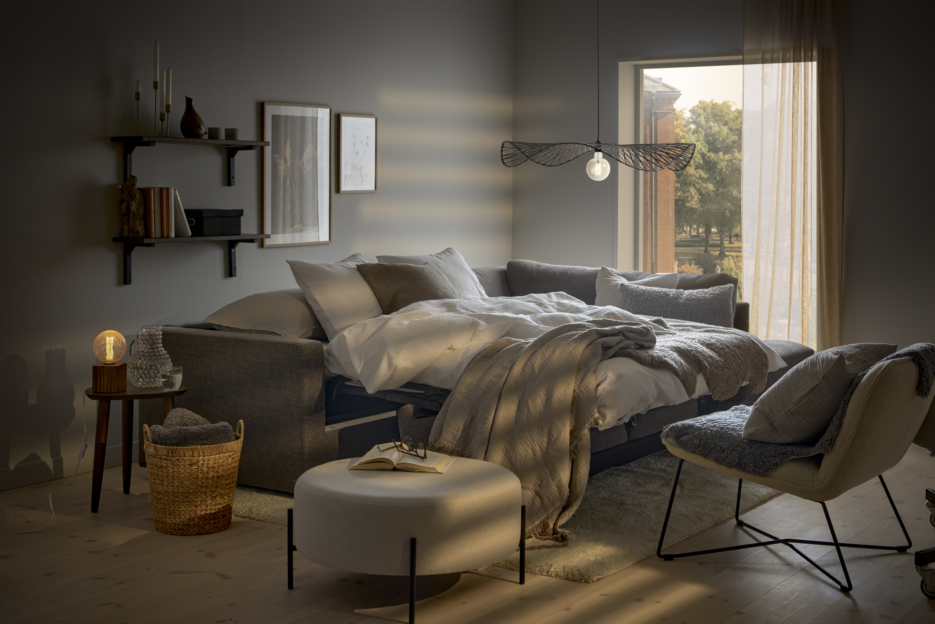 I ett vitt rum står en grå bäddsoffa utbäddad med fluffiga täcken och kuddar