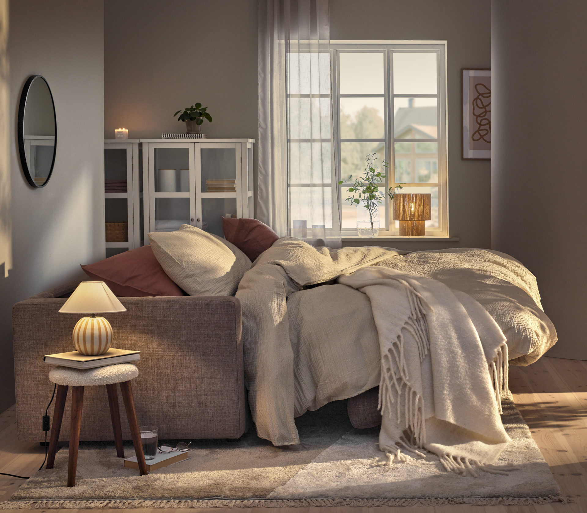 En utfälld bäddsoffa står i ett vardagsrum och är bäddad med beige sängkläder