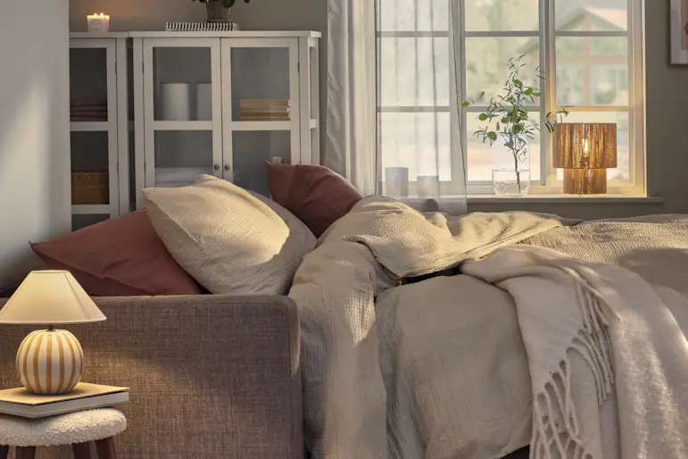 En utfälld bäddsoffa står i ett vardagsrum och är bäddad med beige sängkläder