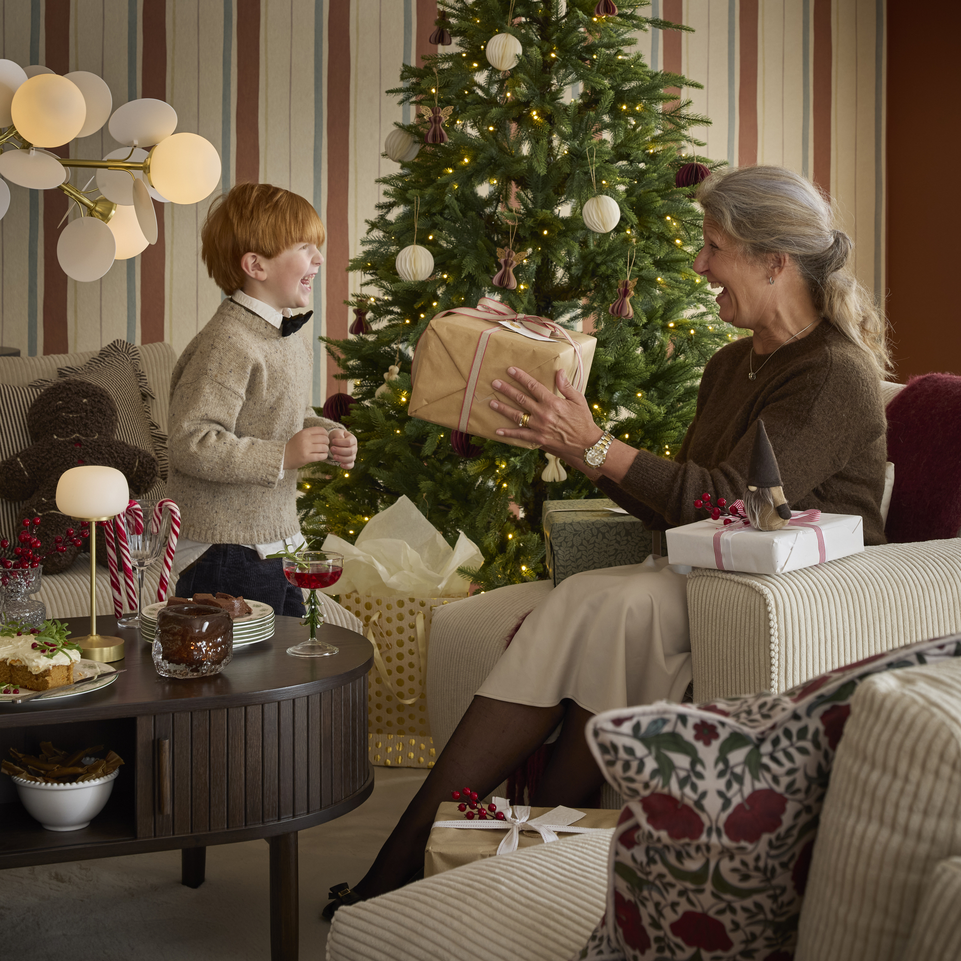 en kvinna och ett barn delar ut julklappar i ett julpyntat hem