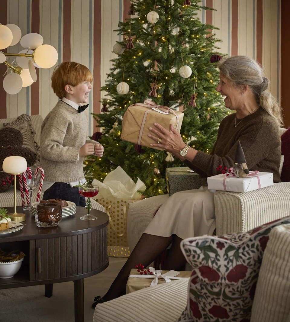 en kvinna och ett barn delar ut julklappar i ett julpyntat hem