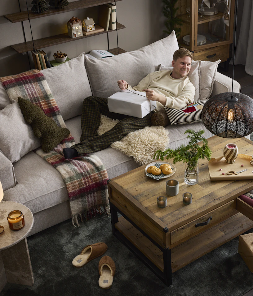 en kille liggandes på en stor grå soffa och håller i en julklapp