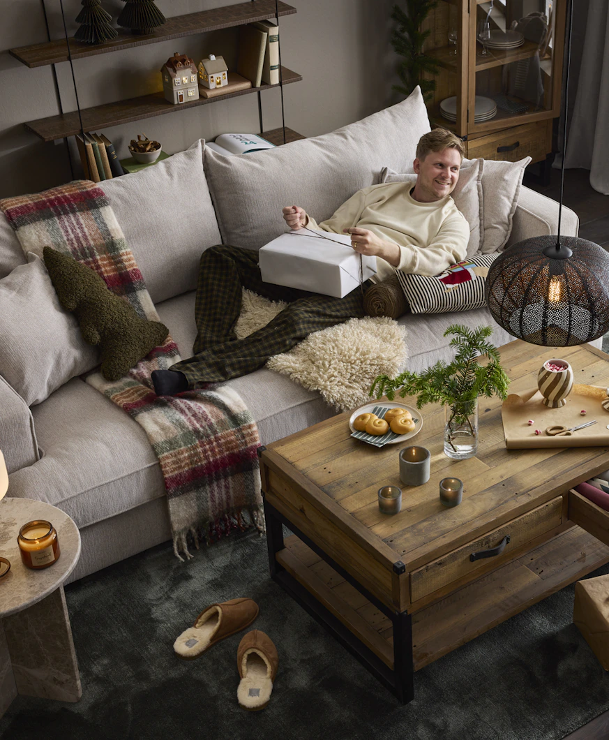 en kille liggandes på en stor grå soffa och håller i en julklapp