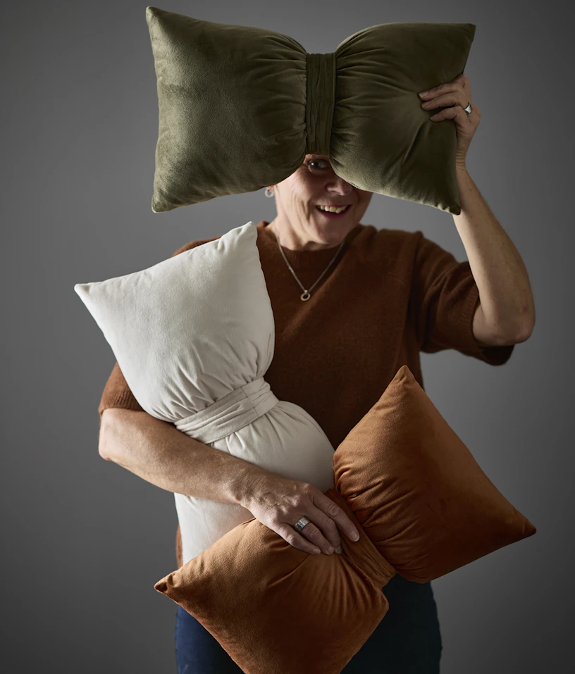 En kvinna håller upp tre prydnadskuddar med form av en rosett