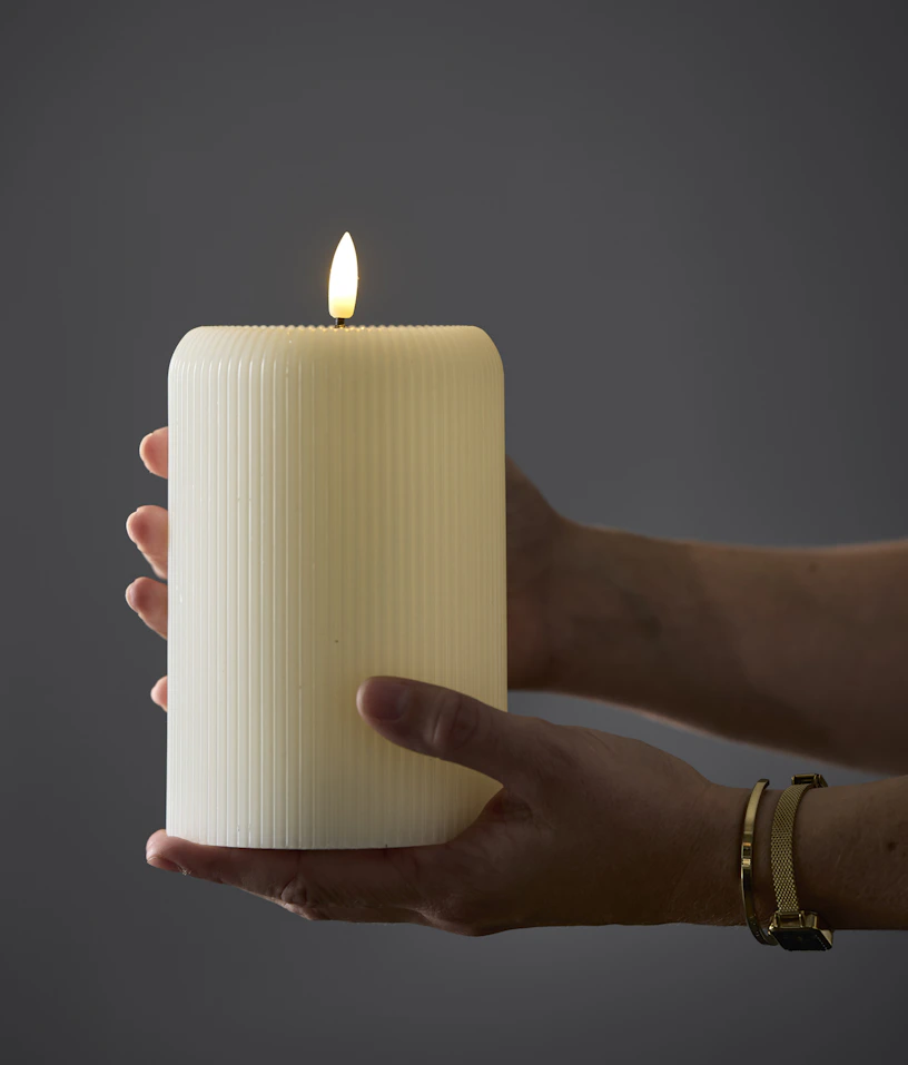 En person håller i ett större LED-ljus med dekorativa ränder