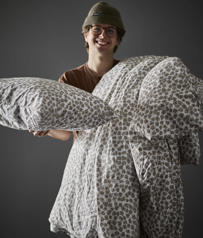 En man håller upp en kudde och ett täcke i blommigt påslakanset