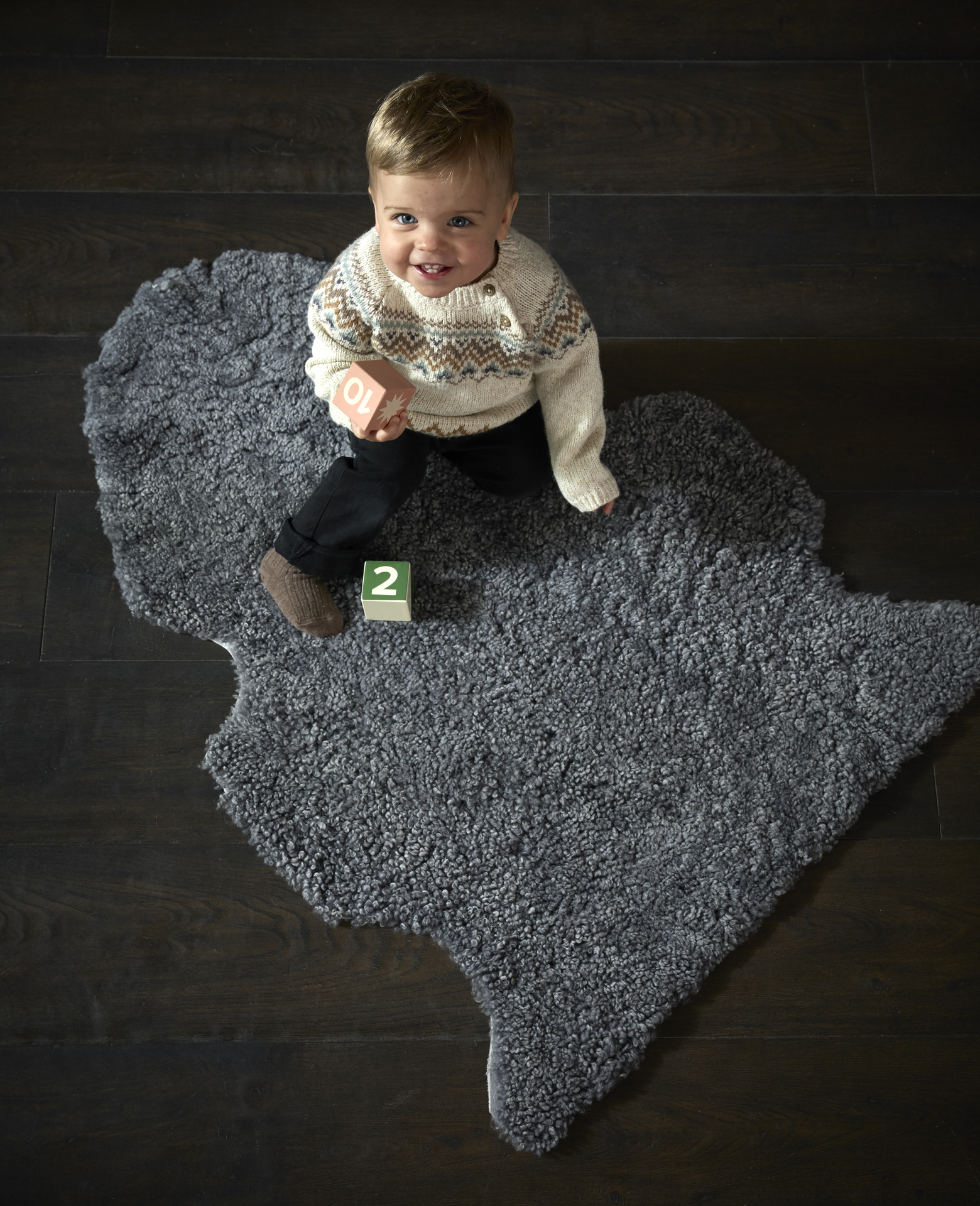 ett barn sittandes på ett grått fårskinn