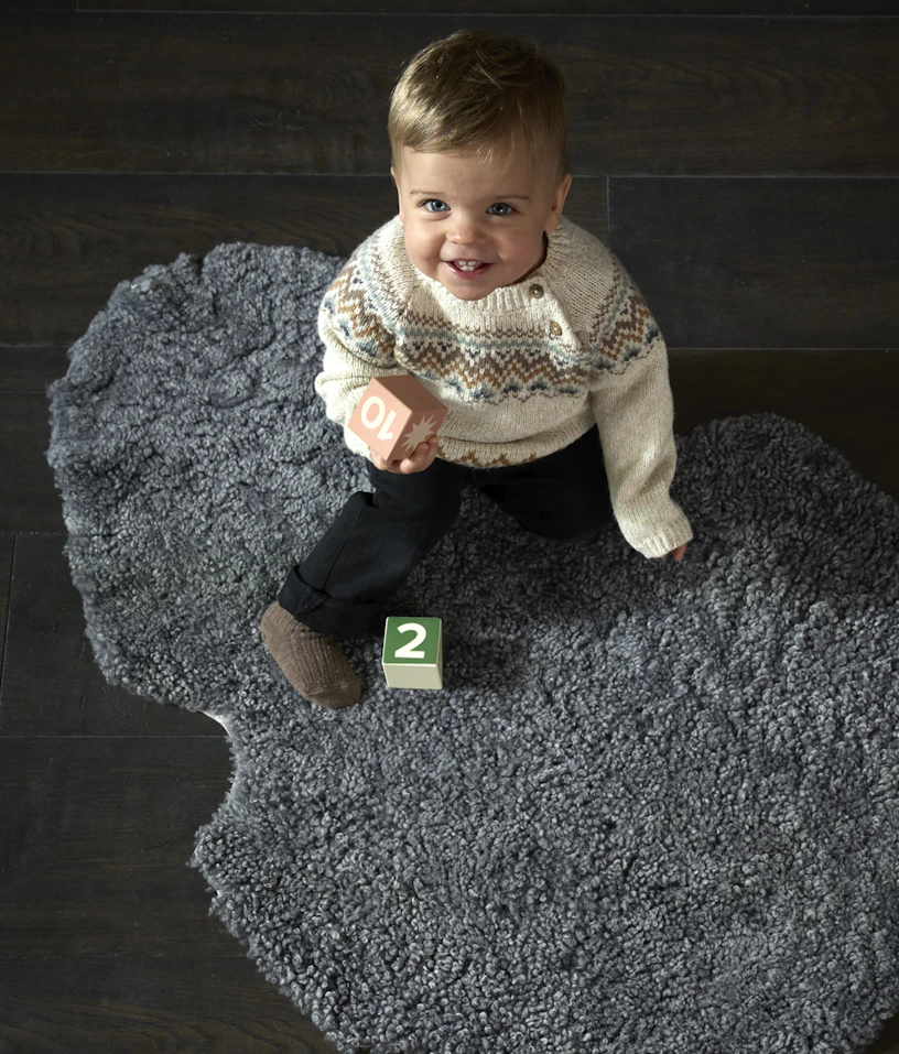 ett barn sittandes på ett grått fårskinn