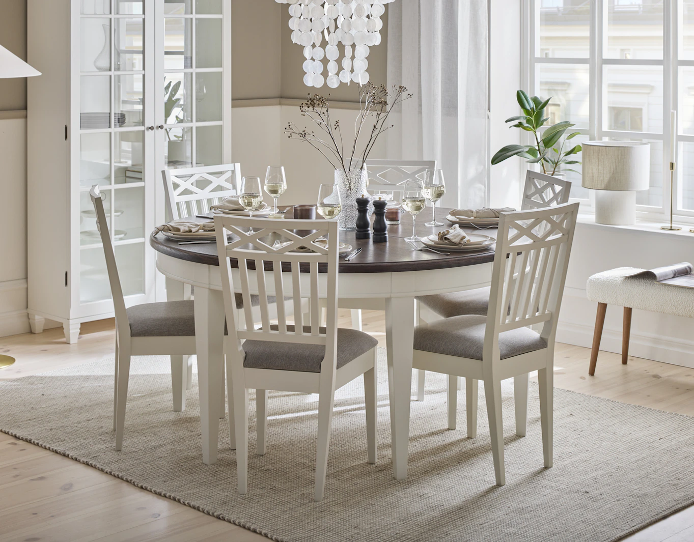 Rum med runt vitt matplatsbord med mörk träskiva med fyra stolar i tygbeklädd sits i klassisk stil.