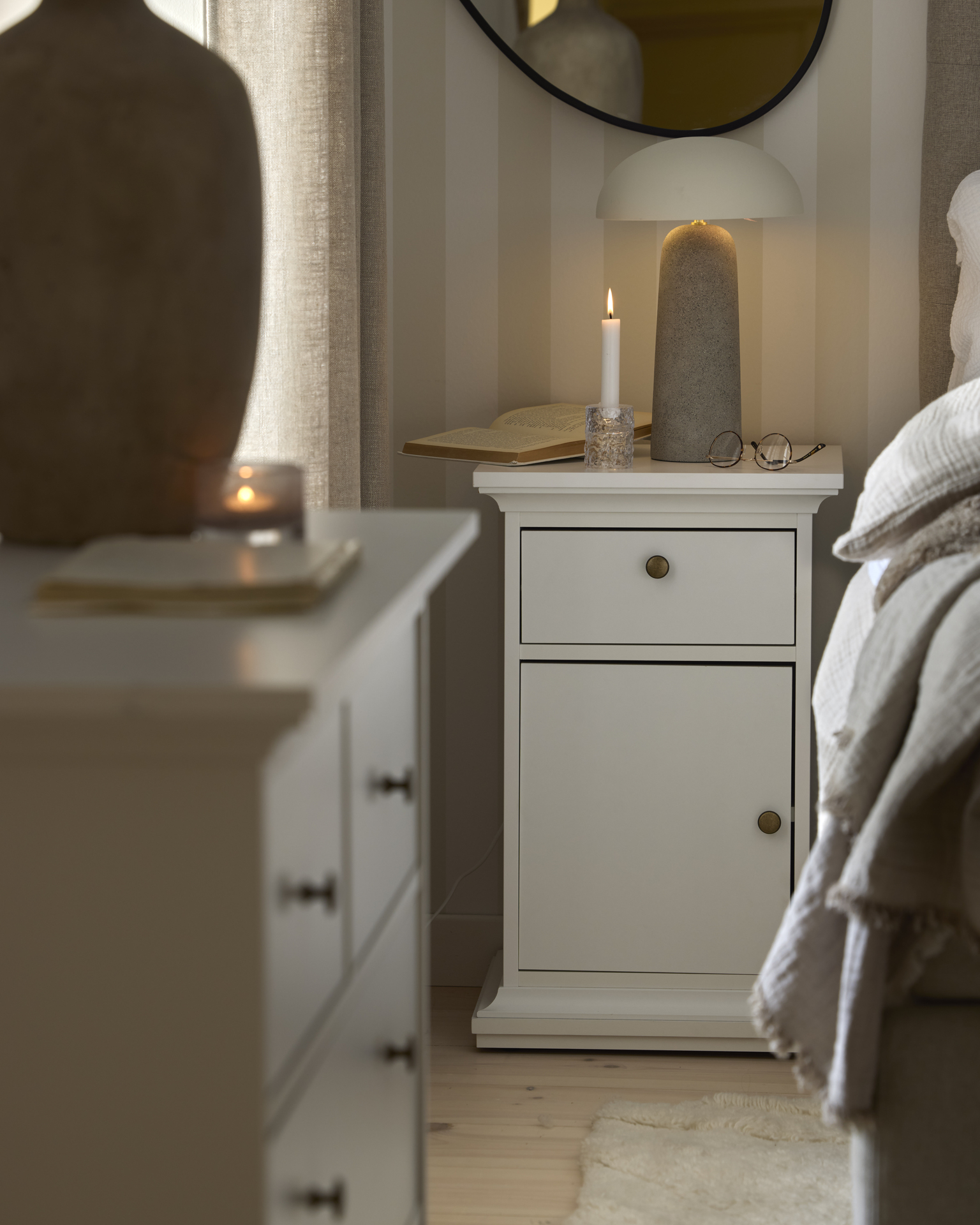 Ett vitt sängbord med en låda och en dörr står bredvid en säng i ett sovrum