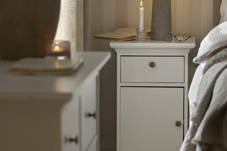 Ett vitt sängbord med en låda och en dörr står bredvid en säng i ett sovrum