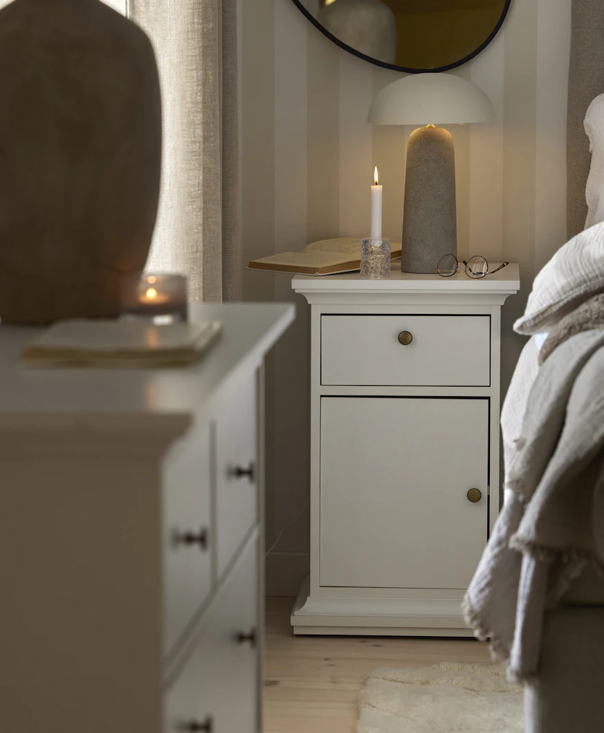 Ett vitt sängbord med en låda och en dörr står bredvid en säng i ett sovrum
