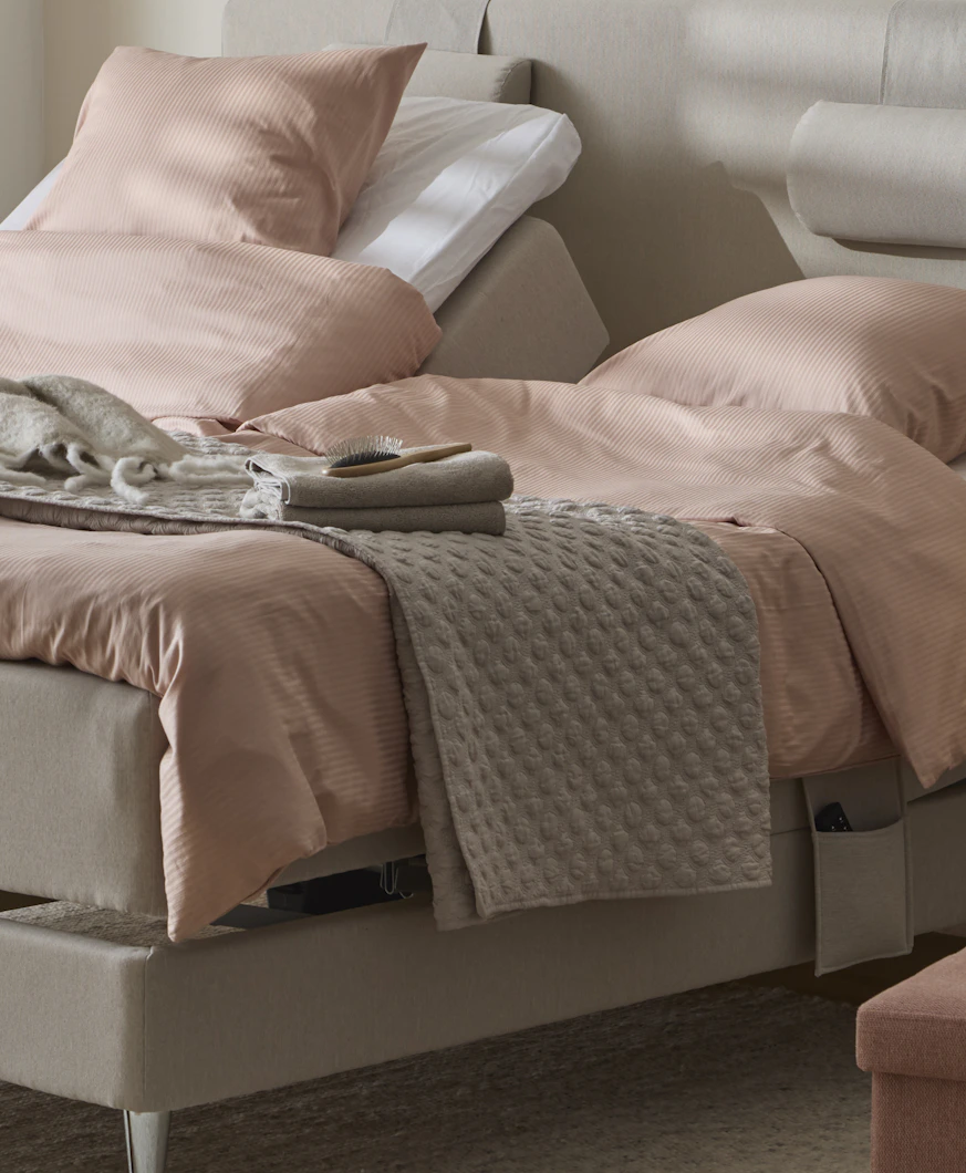 ett grått överkast ligger på en beige säng med rosa sängkläder