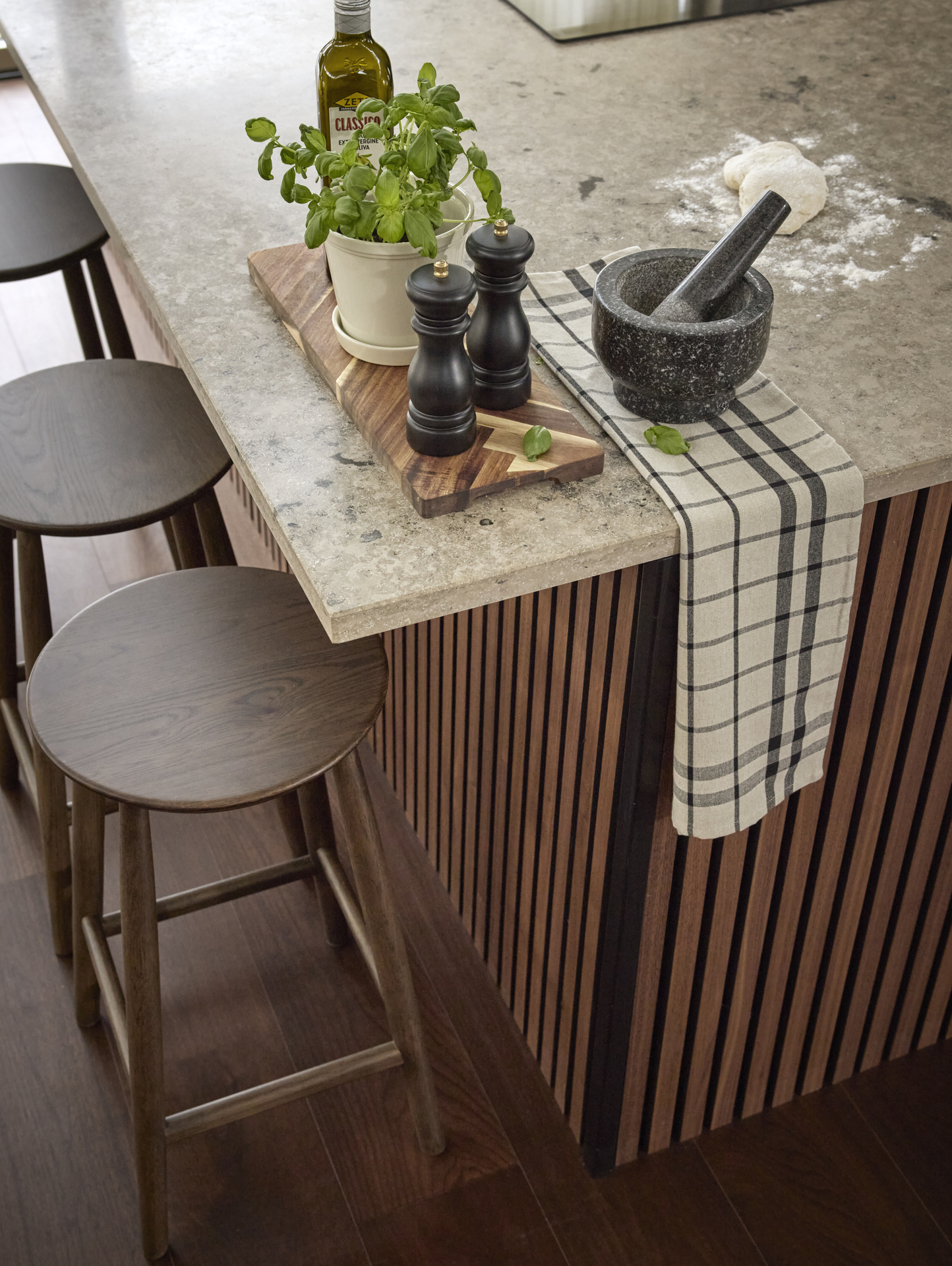 kryddkvarn, olja och basilika i en kruka står på en brun träskärbräda på en köksbänk