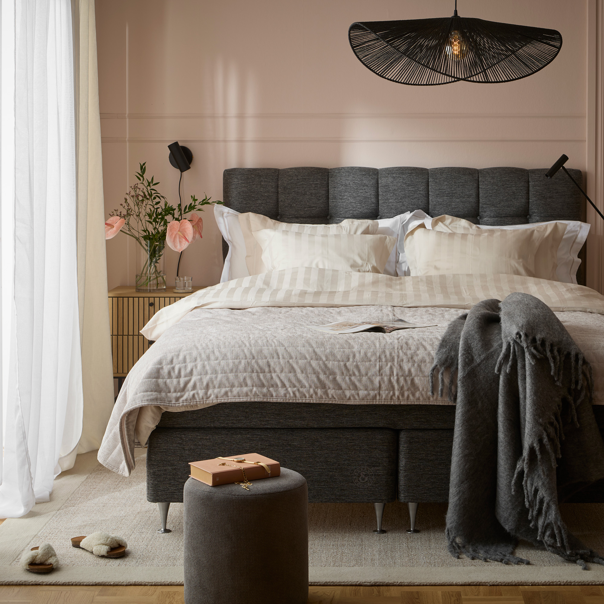 en grå säng i ett sovrum med rosa väggar