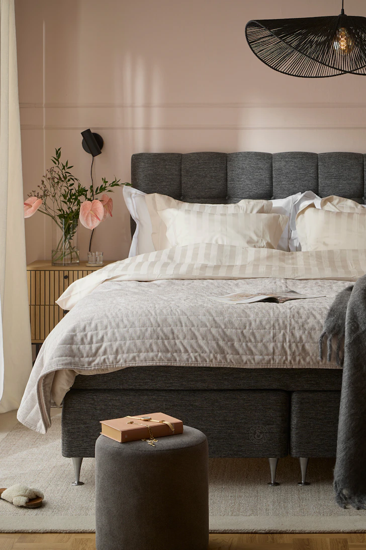 en grå säng i ett sovrum med rosa väggar