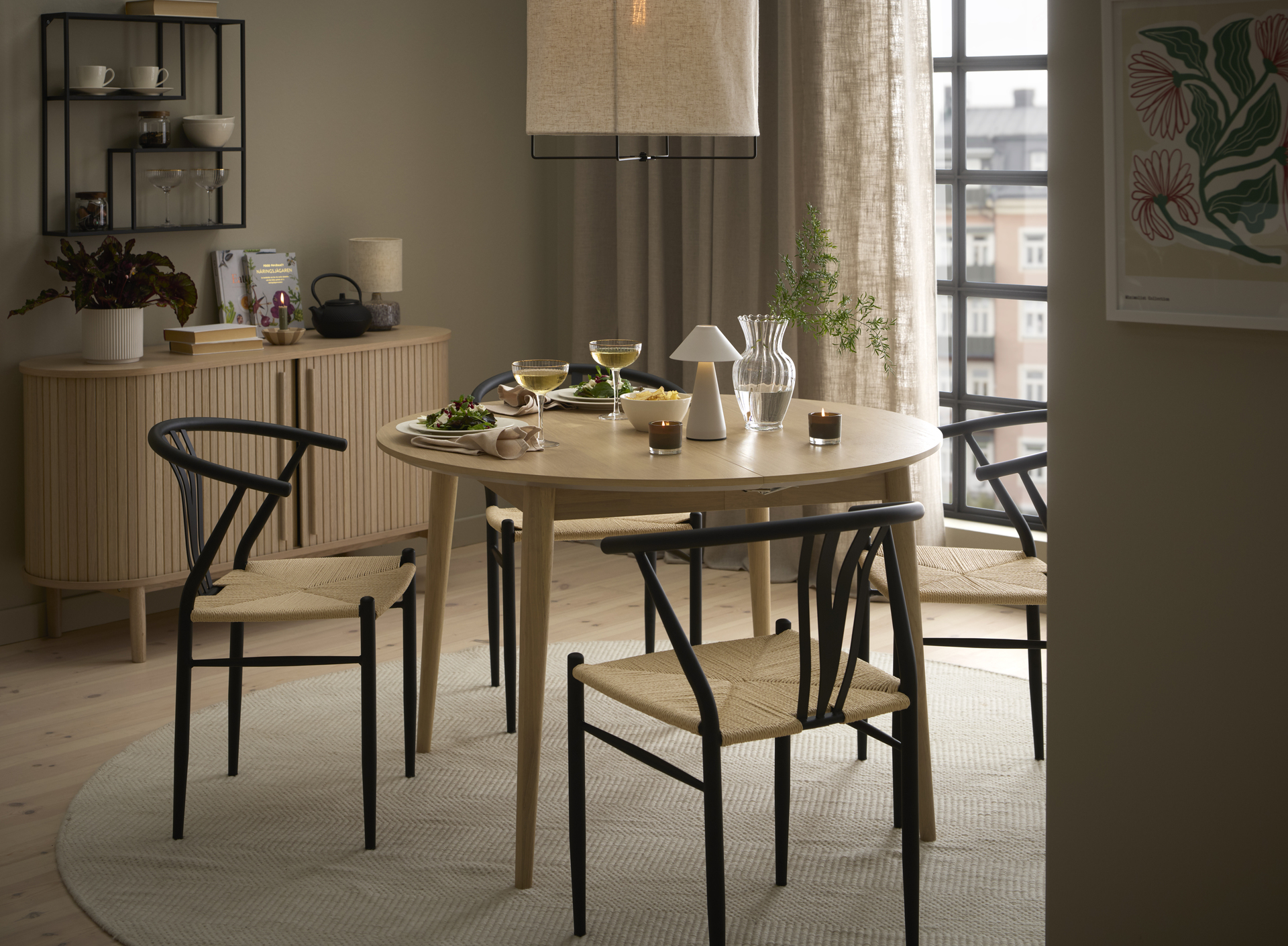Vid ett runt bord i ljust trä står fyra stolar med vävd sits