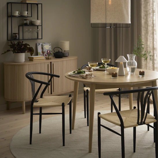 Vid ett runt bord i ljust trä står fyra stolar med vävd sits