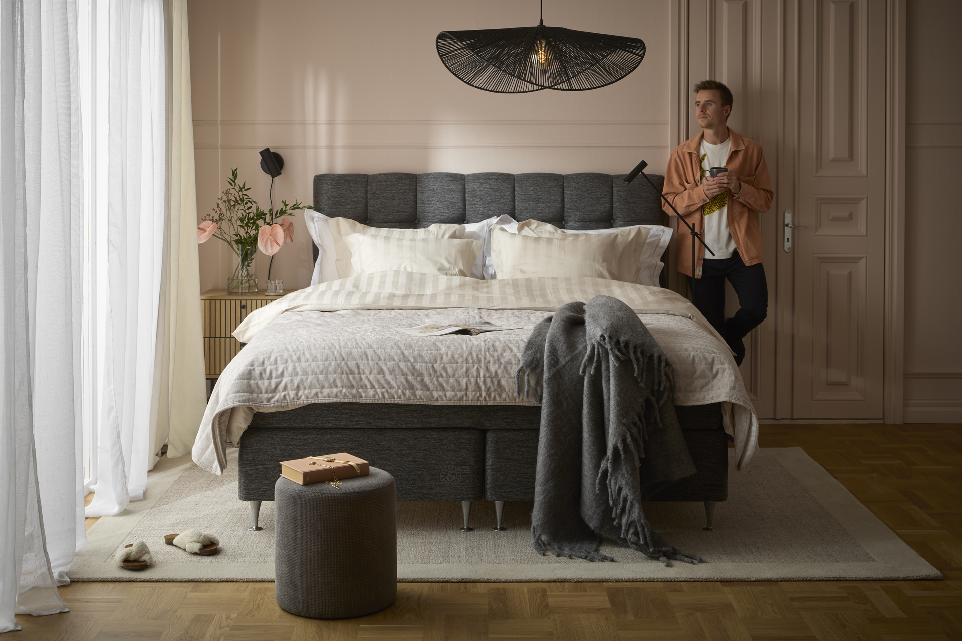 en kille står i ett sovrum med en stor säng och tittar ut genom fönstret