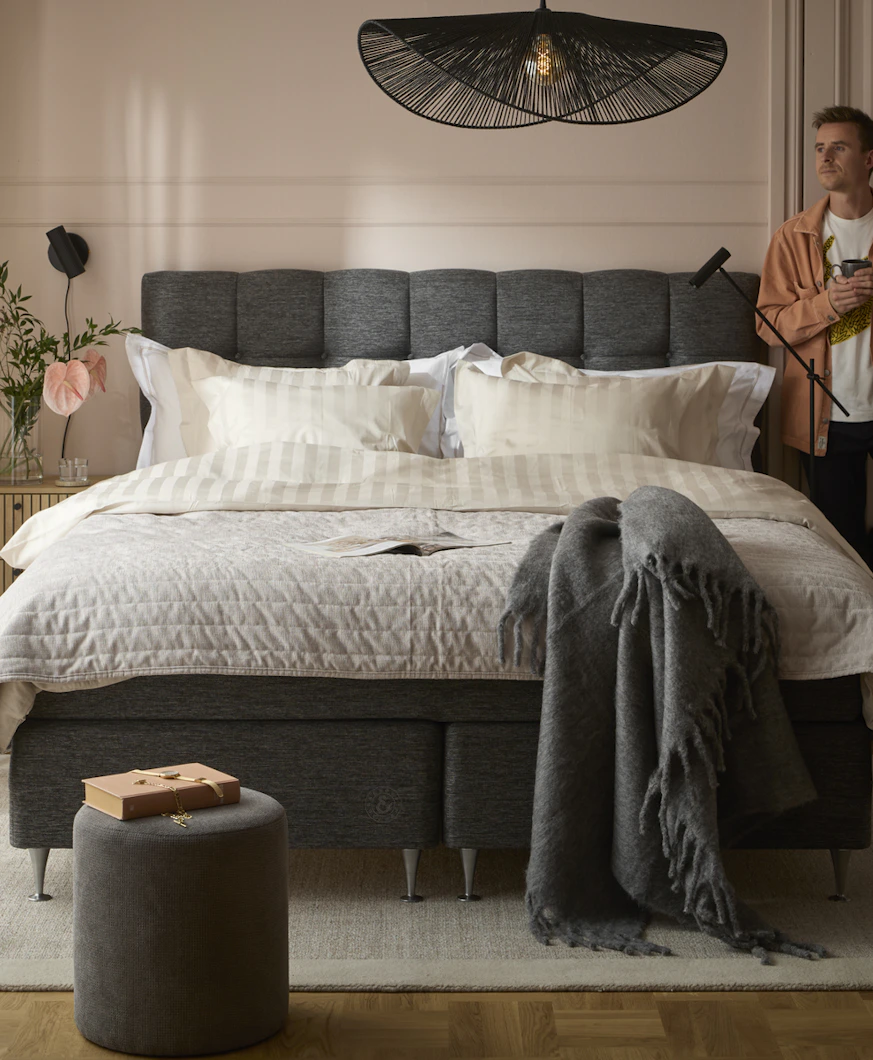 en kille står i ett sovrum med en stor säng och tittar ut genom fönstret