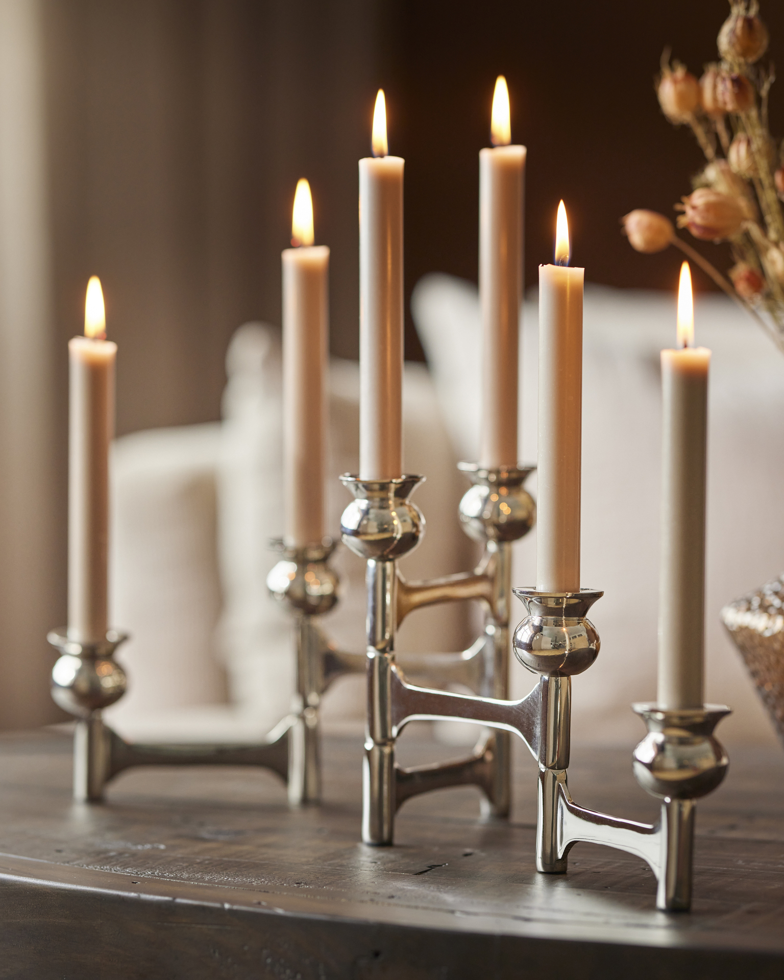 en silvrig ljusstake står på ett bord med flera beiga tända ljus