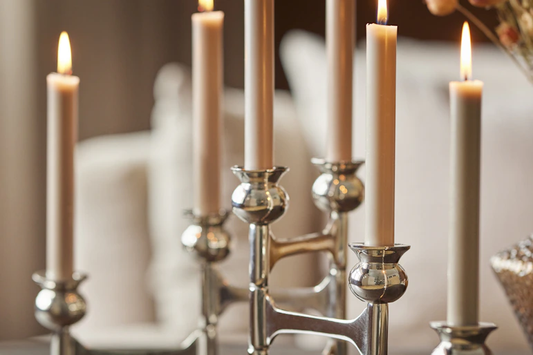 en silvrig ljusstake står på ett bord med flera beiga tända ljus