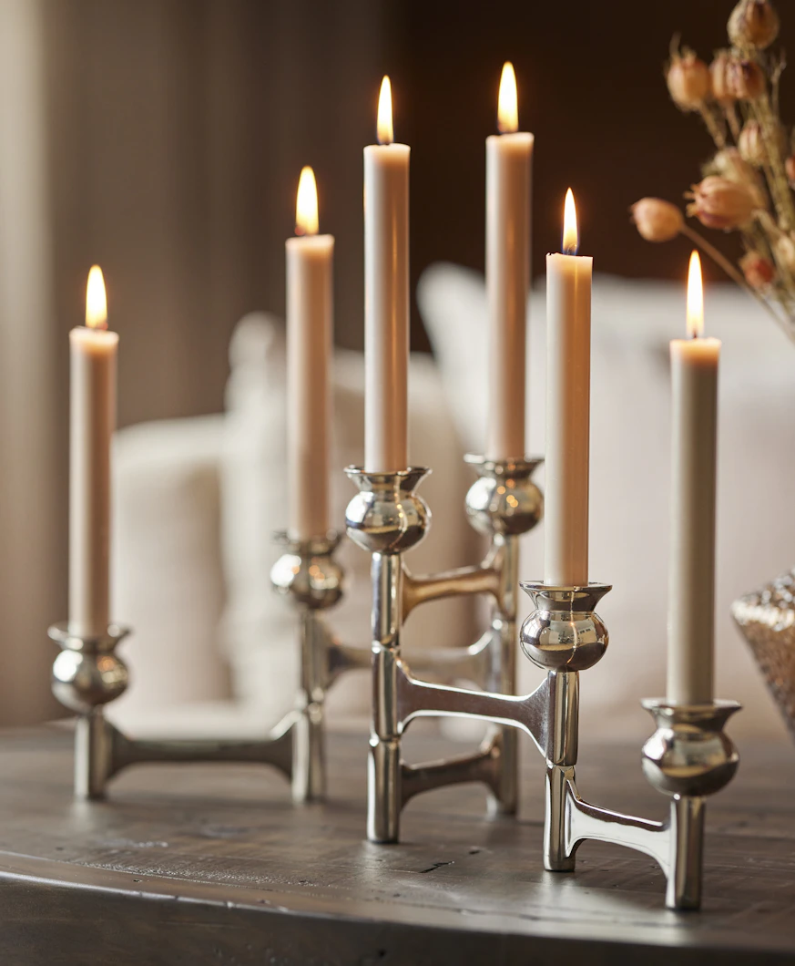 en silvrig ljusstake står på ett bord med flera beiga tända ljus