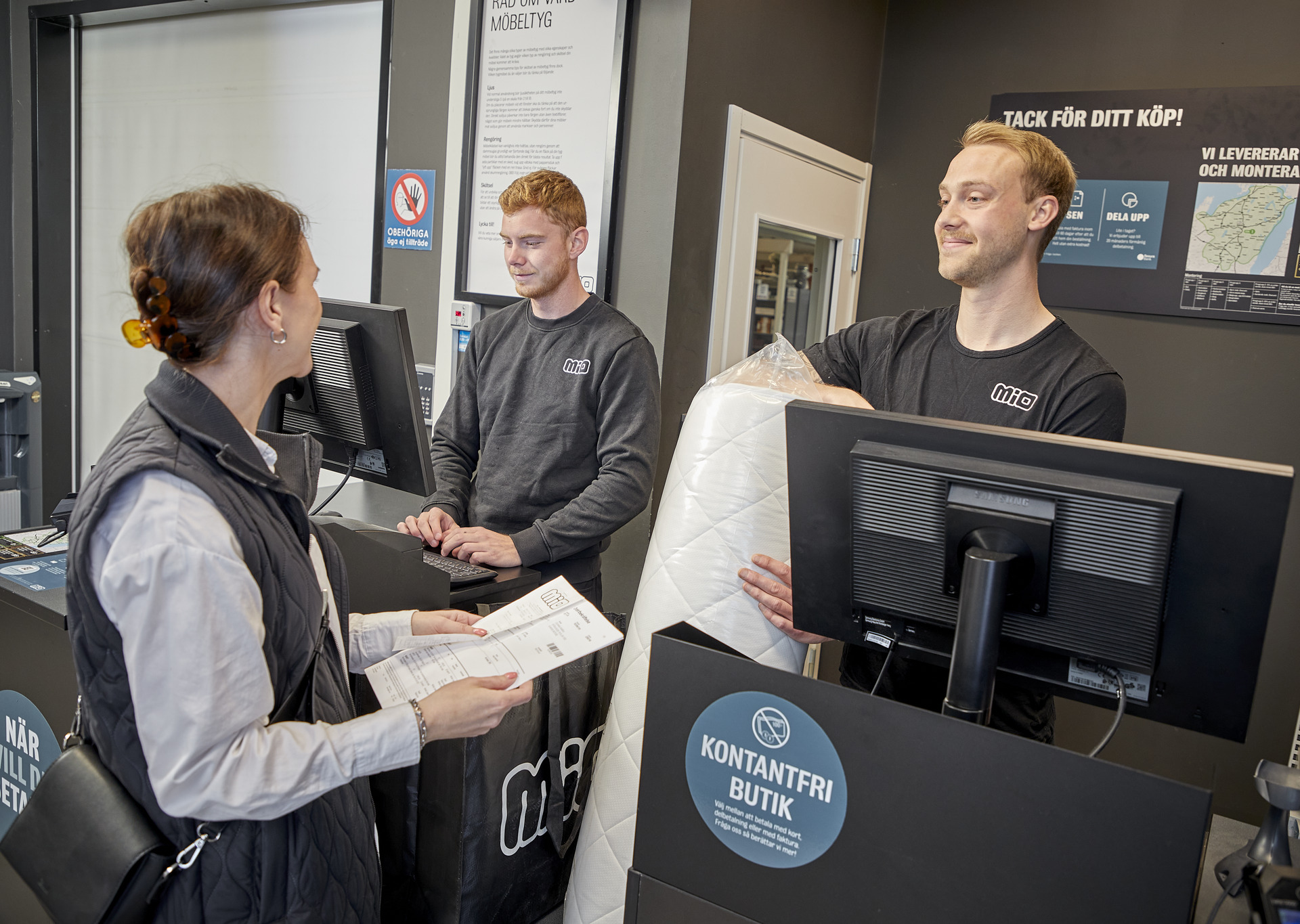 Manlig butiksmedarbetare pratar leende med kund vid kassadisken. 