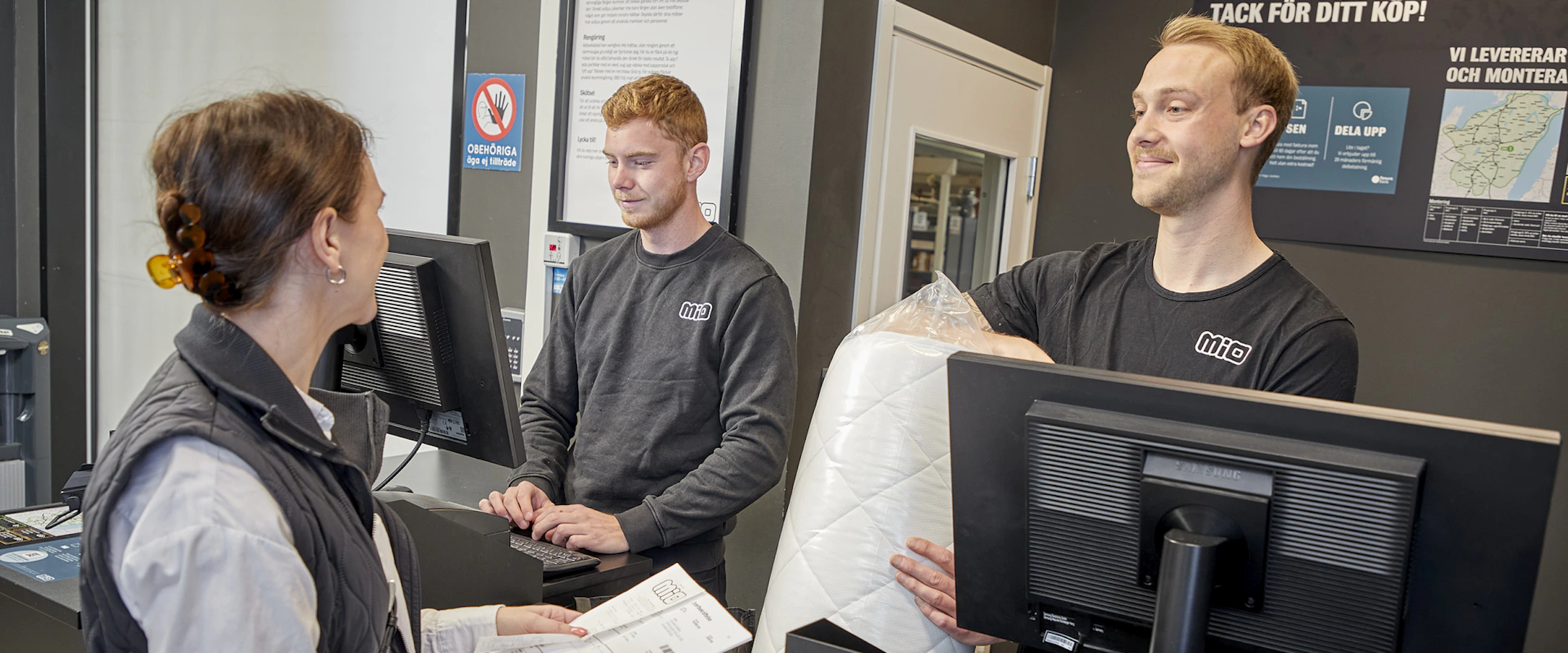 Manlig butiksmedarbetare pratar leende med kund vid kassadisken.