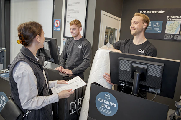 Manlig butiksmedarbetare pratar leende med kund vid kassadisken.