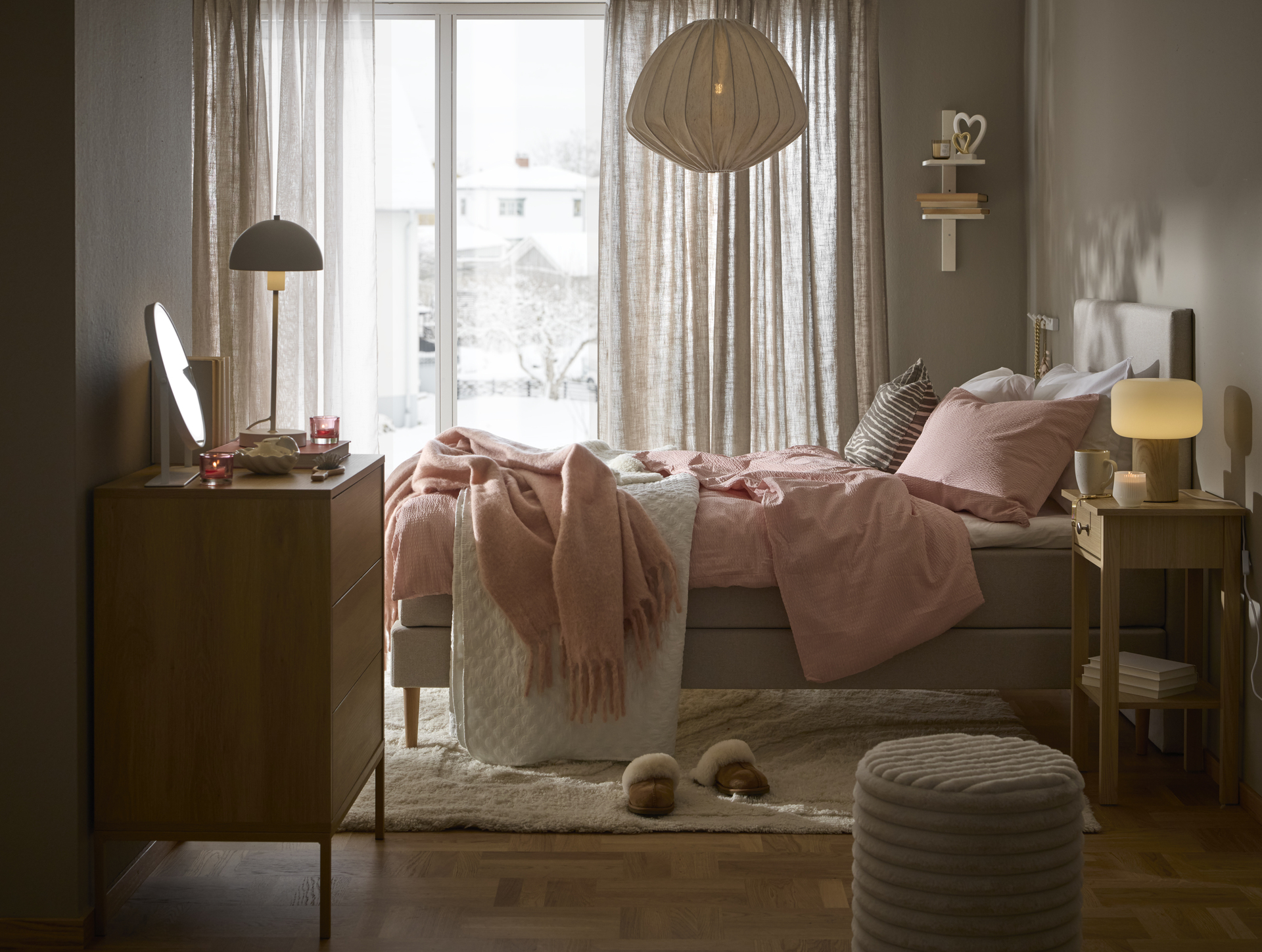 ljusgrå mindre säng står i ett skandinaviskt sovrum med ljust rosa påslakanset liggandes över sängen. 