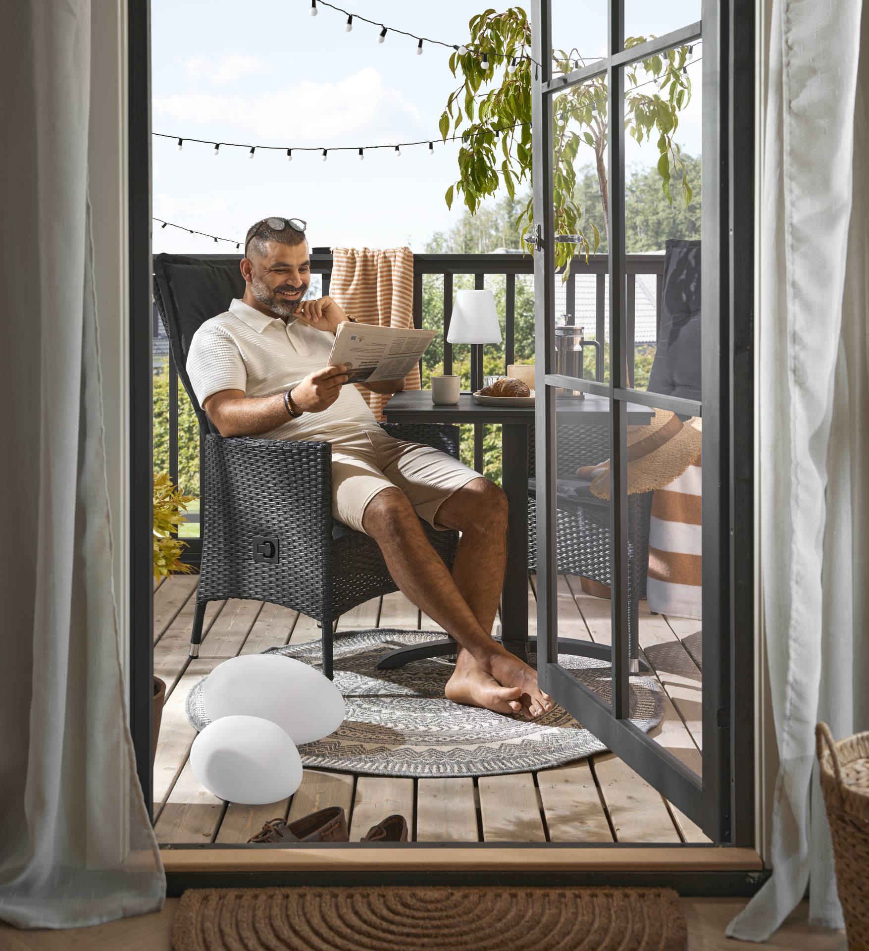 PÅ en balkong sitter en man i en stol och läser tidningen