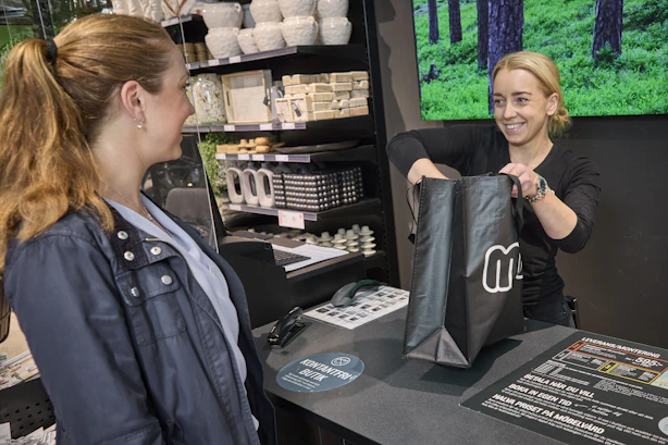 Kvinnlig butiksarbetare hjälper kund att plocka ner varor i shoppingpåse vid kassan i Miobutik.