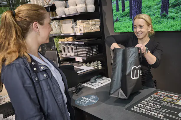 Kvinnlig butiksarbetare hjälper kund att plocka ner varor i shoppingpåse vid kassan i Miobutik.