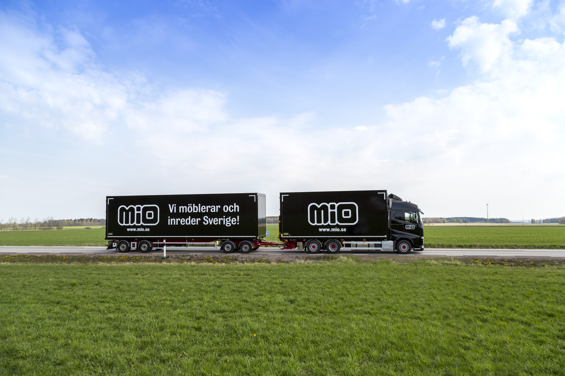 Svart lastbil med släp med Miologotyper på sidan och texten "Vi möblerar och inreder Sverige"