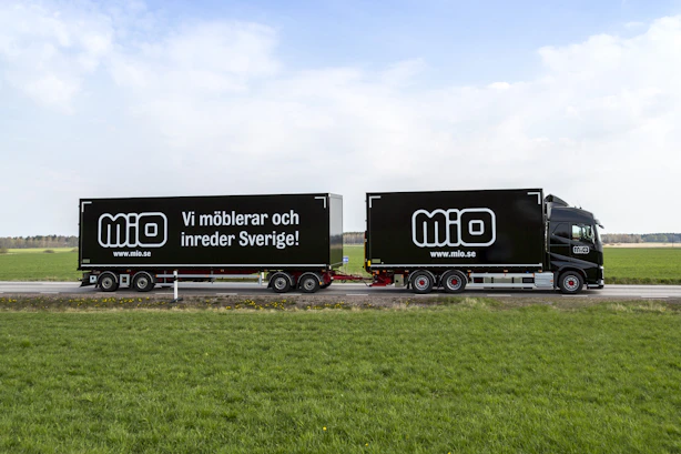 Svart lastbil med släp med Miologotyper på sidan och texten "Vi möblerar och inreder Sverige"
