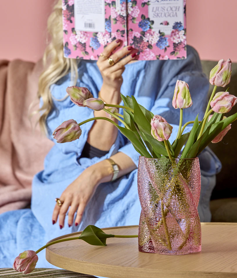 En rosa vas med rosa tulpaner står på ett soffbord i ljust trä