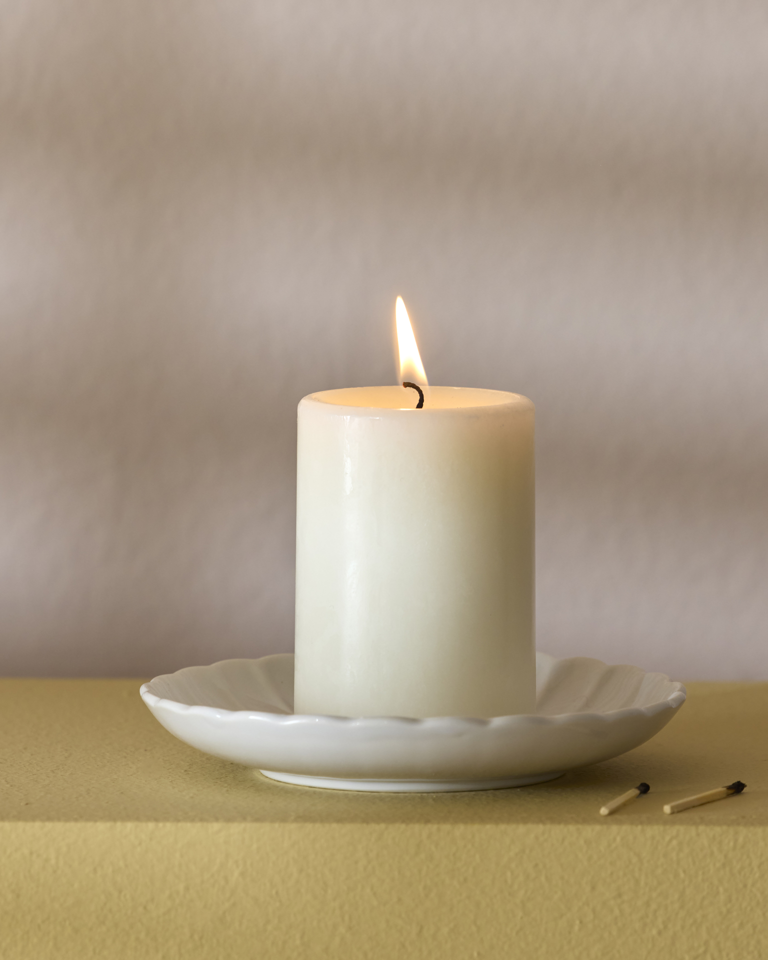 ett vitt blockljus är tänt och står på ett vitt runt fat