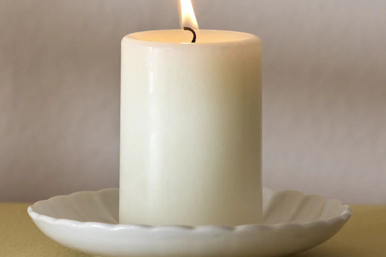 ett vitt blockljus är tänt och står på ett vitt runt fat