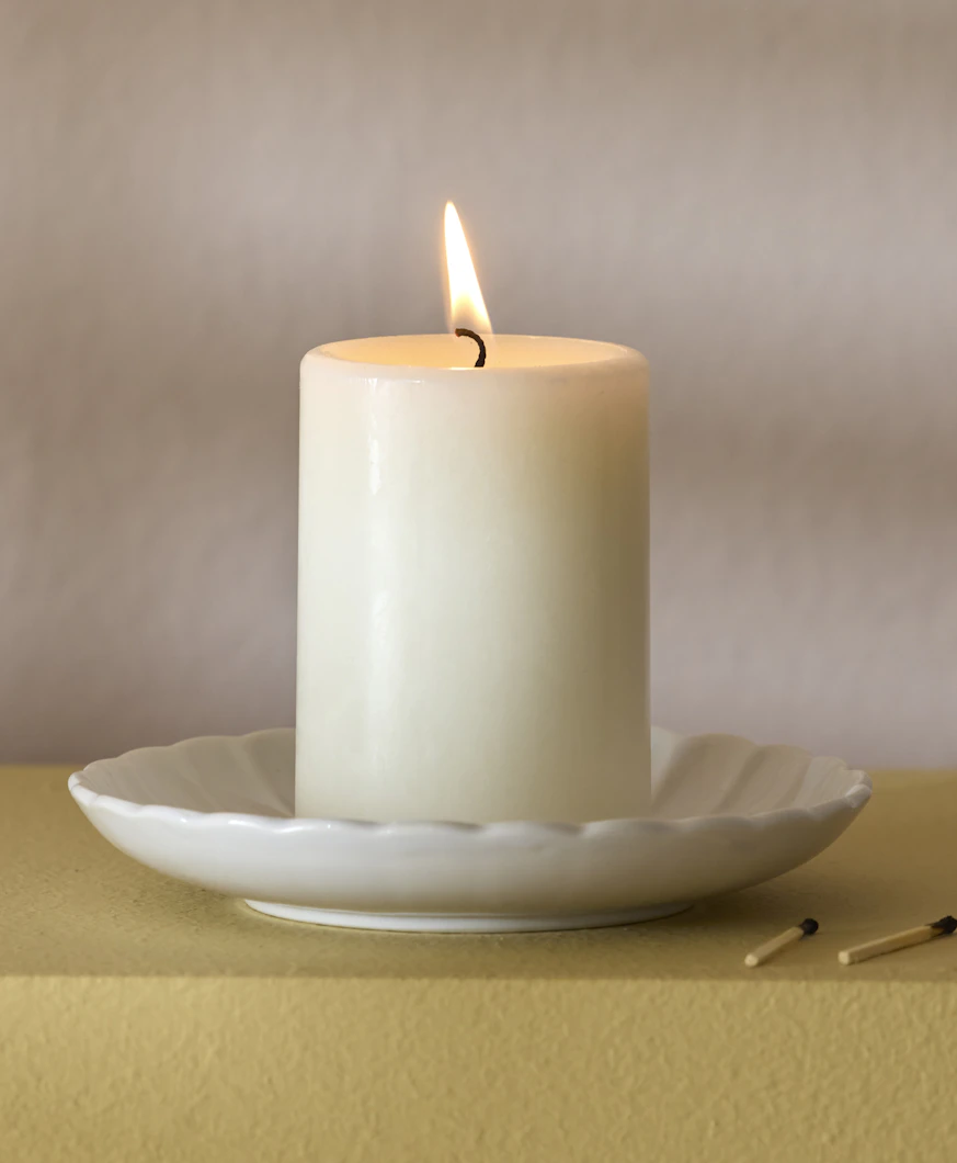 ett vitt blockljus är tänt och står på ett vitt runt fat