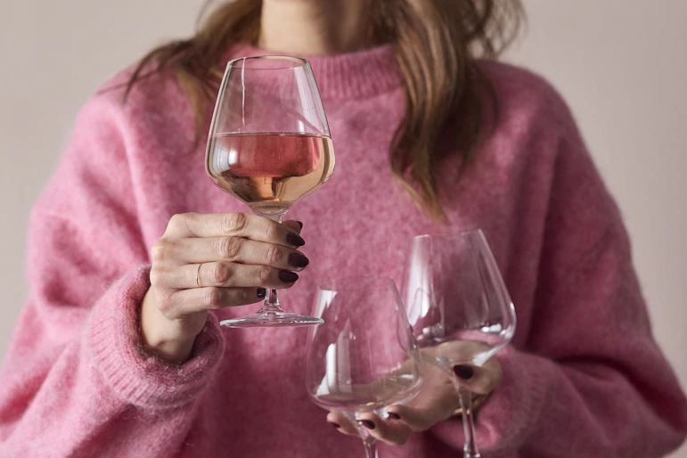 en tjej håller fram tre vinglas framför sin rosa tröja