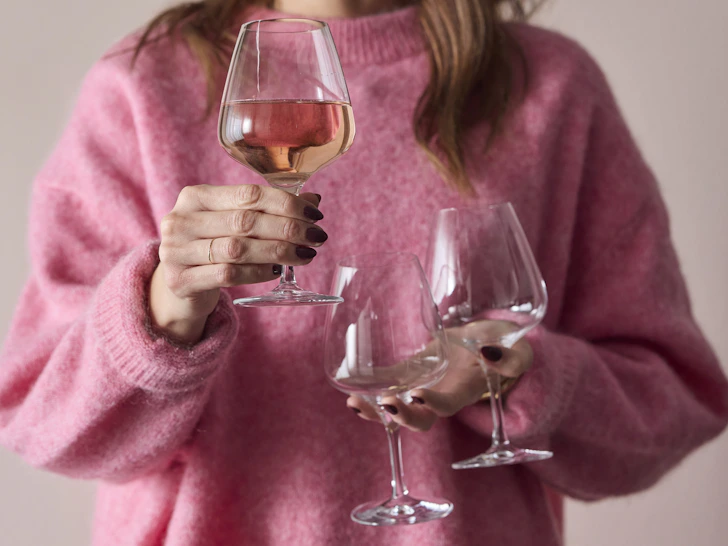 en person som håller fram tre vinglas framför sin rosa tröja