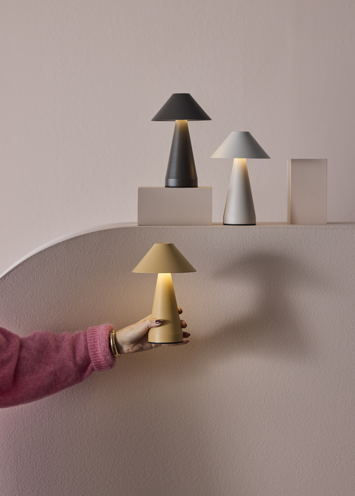 En hand håller i en gul portabel lampa emot en ljusrosa fondvägg