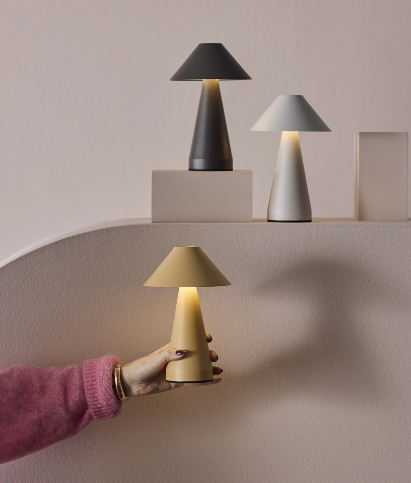 En hand håller i en gul portabel lampa emot en ljusrosa fondvägg