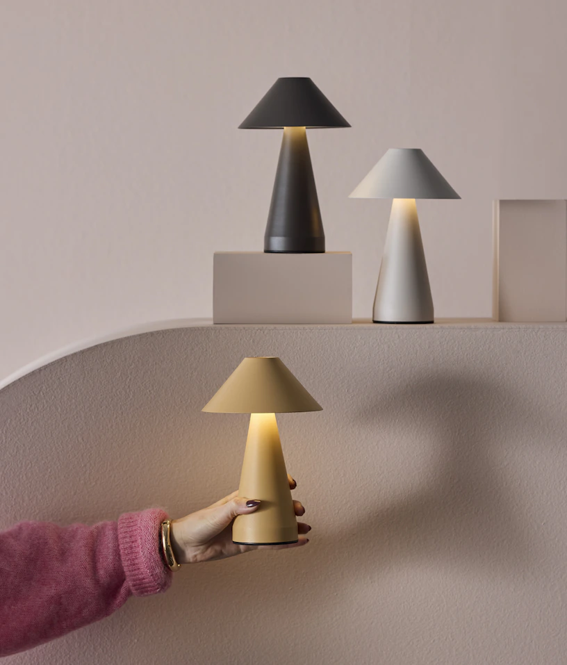 En hand håller i en gul portabel lampa emot en ljusrosa fondvägg